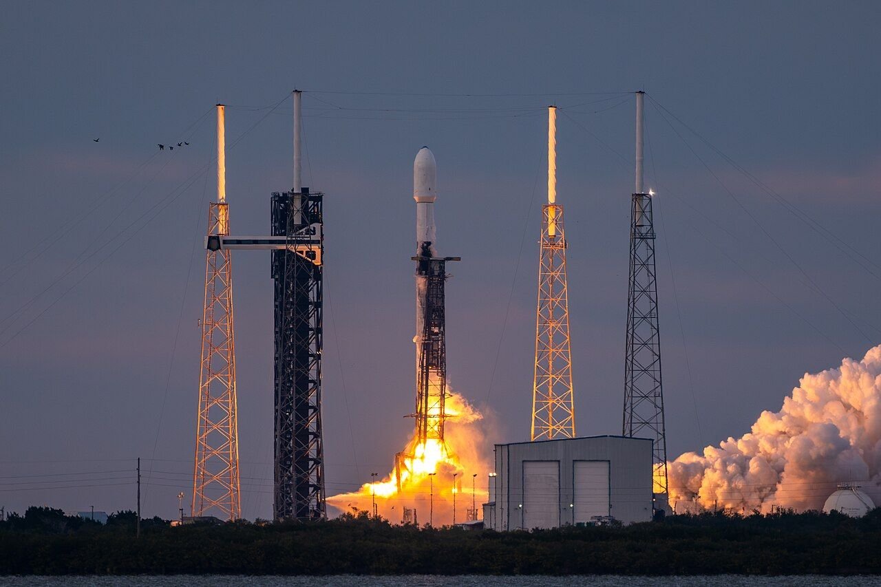 A SpaceX Falcon 9 rocket lifting off from the launch pad at Cape Canaveral, with exhaust clouds and lightning towers around it